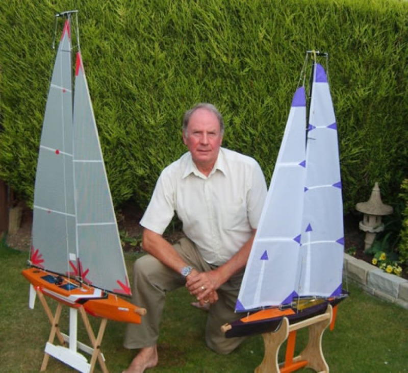 John Goodyear sitting on the grass with his two model yachts, one on each side, Location: England