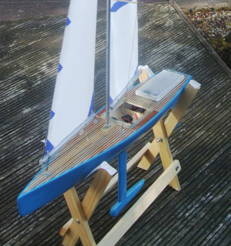 Looking down at a model yacht with pinned striped deck and blue hull sitting on a cradle, Location: UK