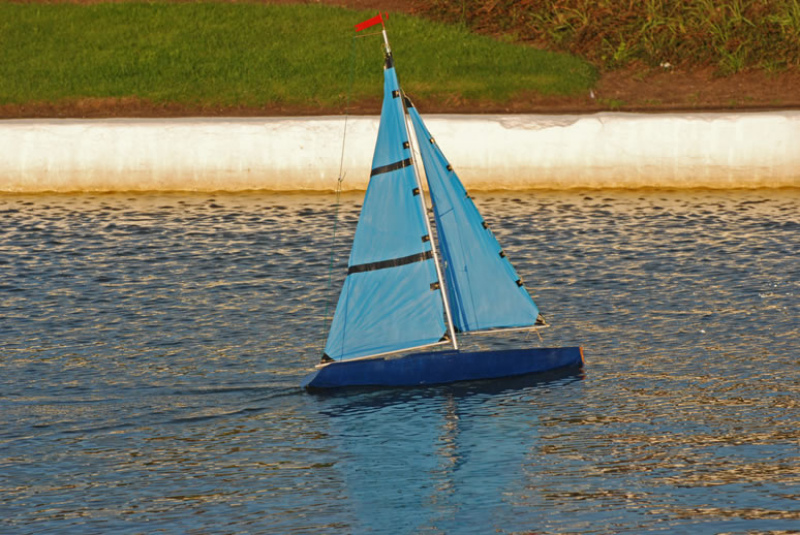 A blue one meter racing sparrow model yacht, sails look rustic and the boat is sailing fast on the lake, Location: Ayrshire, Scotland