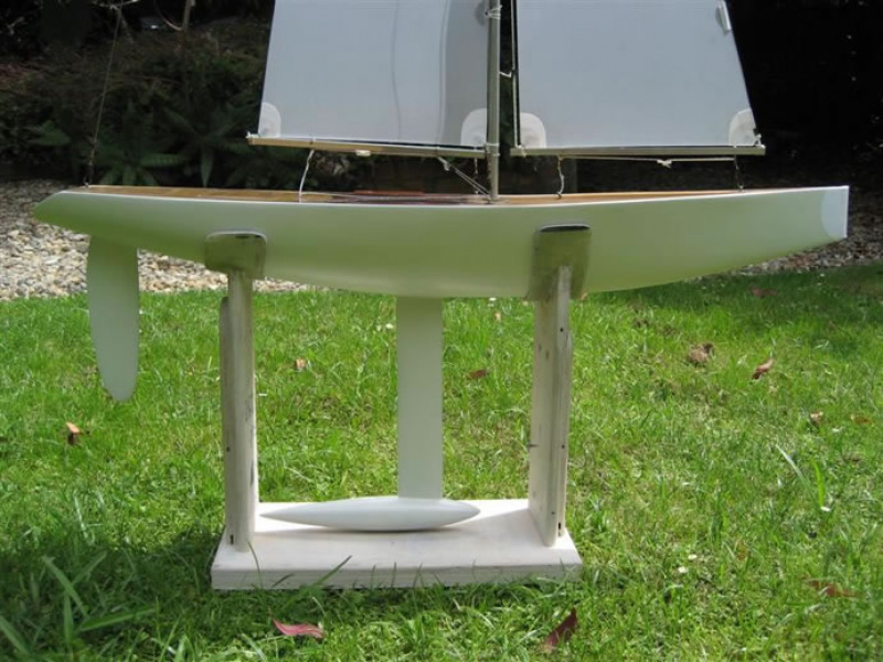 A side on view of a white model yacht, sitting on a cradle on a green lawn, Location: Auckland, New Zealand