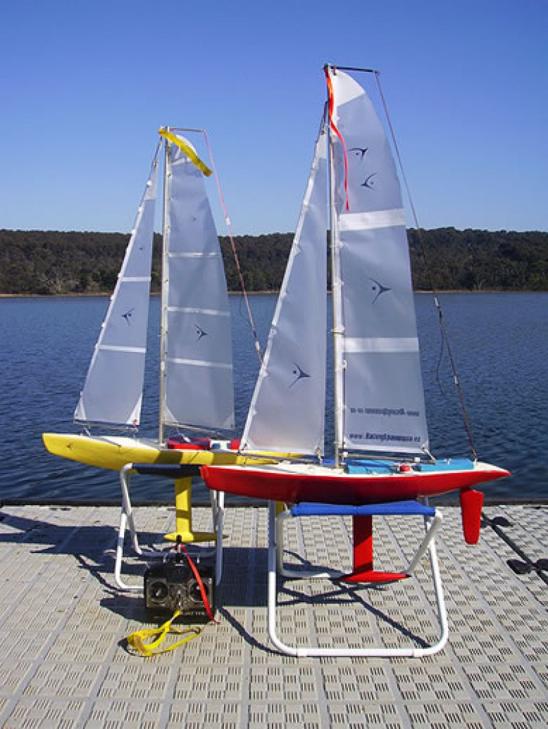 One red and one yellow model yacht sitting on a pontoon about to go sailing, Location: Australia