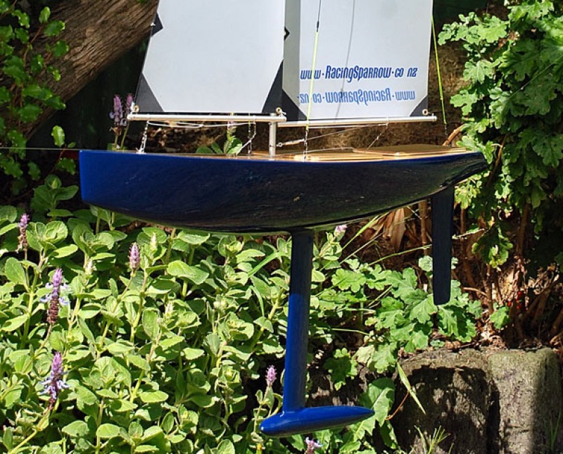 John Sheehan's dark navy blue racing sparrow model yacht. Very shiney and highly polished, sitting in the backyard