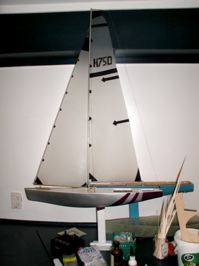 A silver and purple model yacht with a white keel sitting on a work bench. Behind this can be seen a blue model yacht hull, the prototype model used for racing sparrow testing