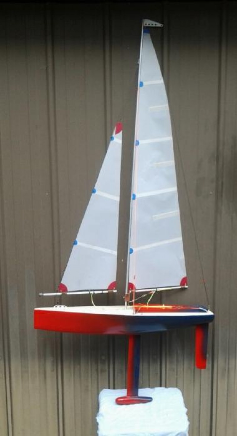 A red to blue gradient paint job on a model yacht hull, the boat sitting against a wall on display with a large lead bulb keel