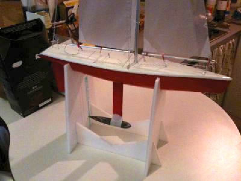 A small rc yacht red in colour sitting in a small styrene cradle on a table